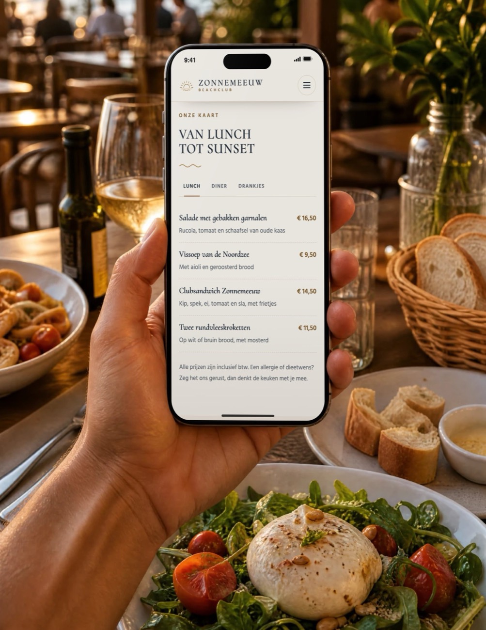 Telefoon met de menukaart van voorbeeldsite Beachclub Zonnemeeuw, op een tafel met pasta, wijn, brood en een salade